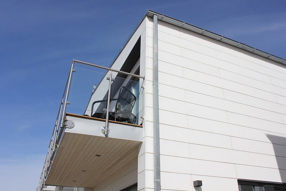 Modern white building with small balcony, metal railing, and blue sky background.