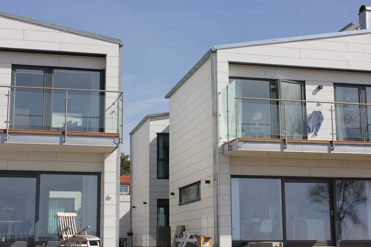 Modern white buildings with large windows, balconies, and a clear blue sky.