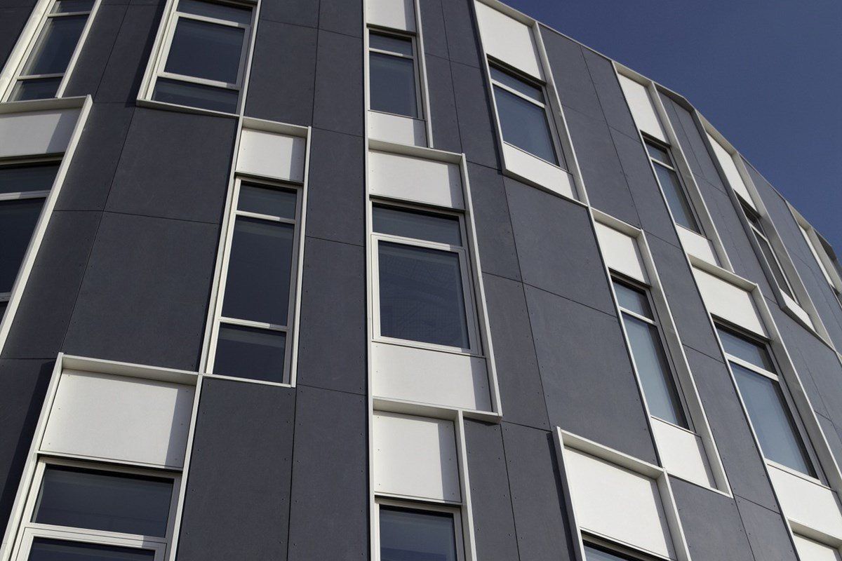 Modern building exterior with dark gray and white paneling and rectangular windows against a blue sky.