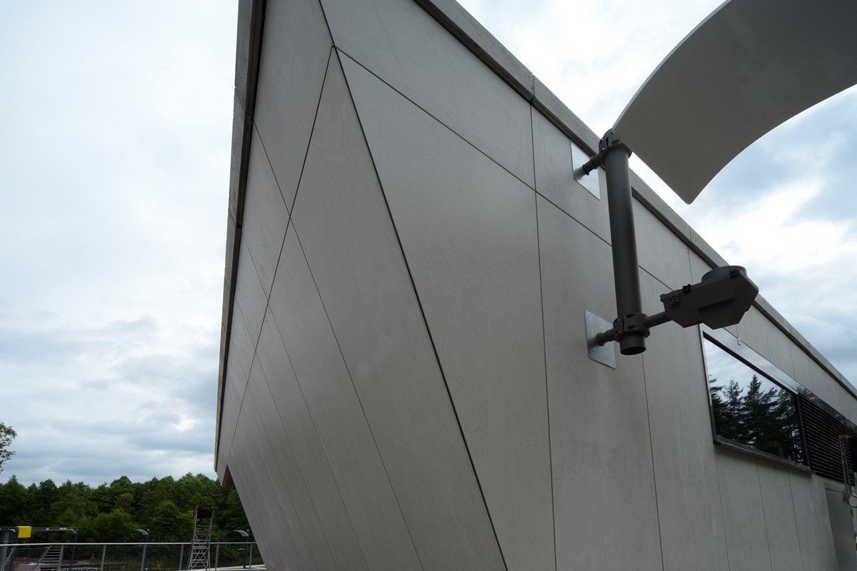 Off-white building exterior with geometric panels and dark trim against a cloudy sky.