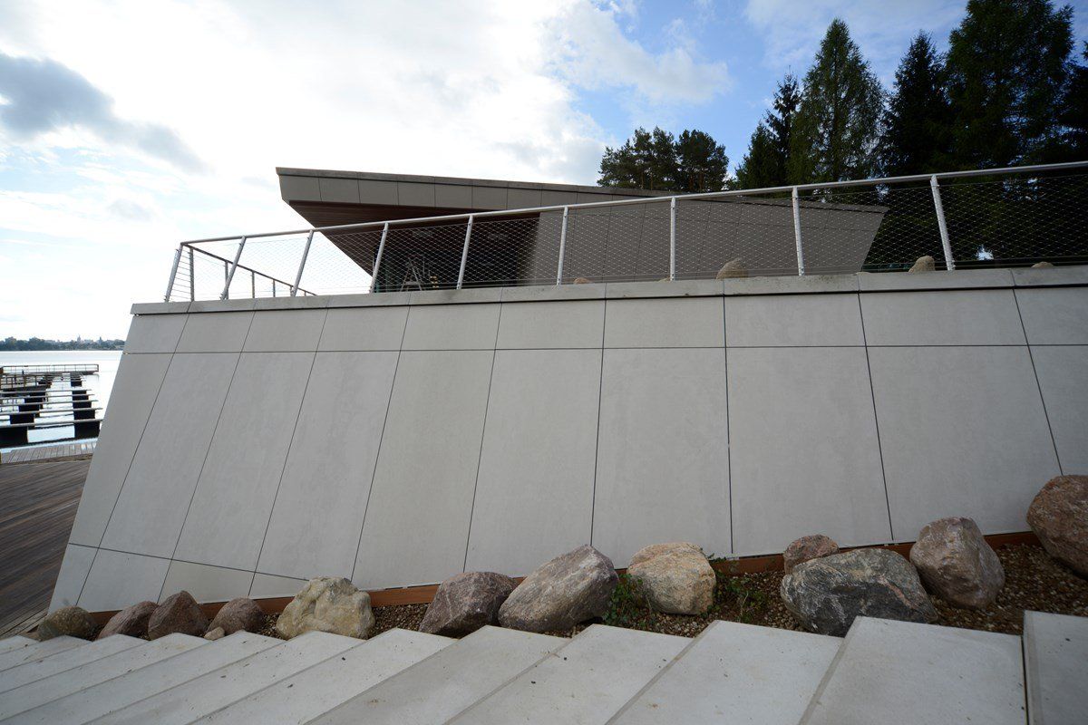 A modern, white concrete building with a railing, rocks at its base, and a cloudy sky.