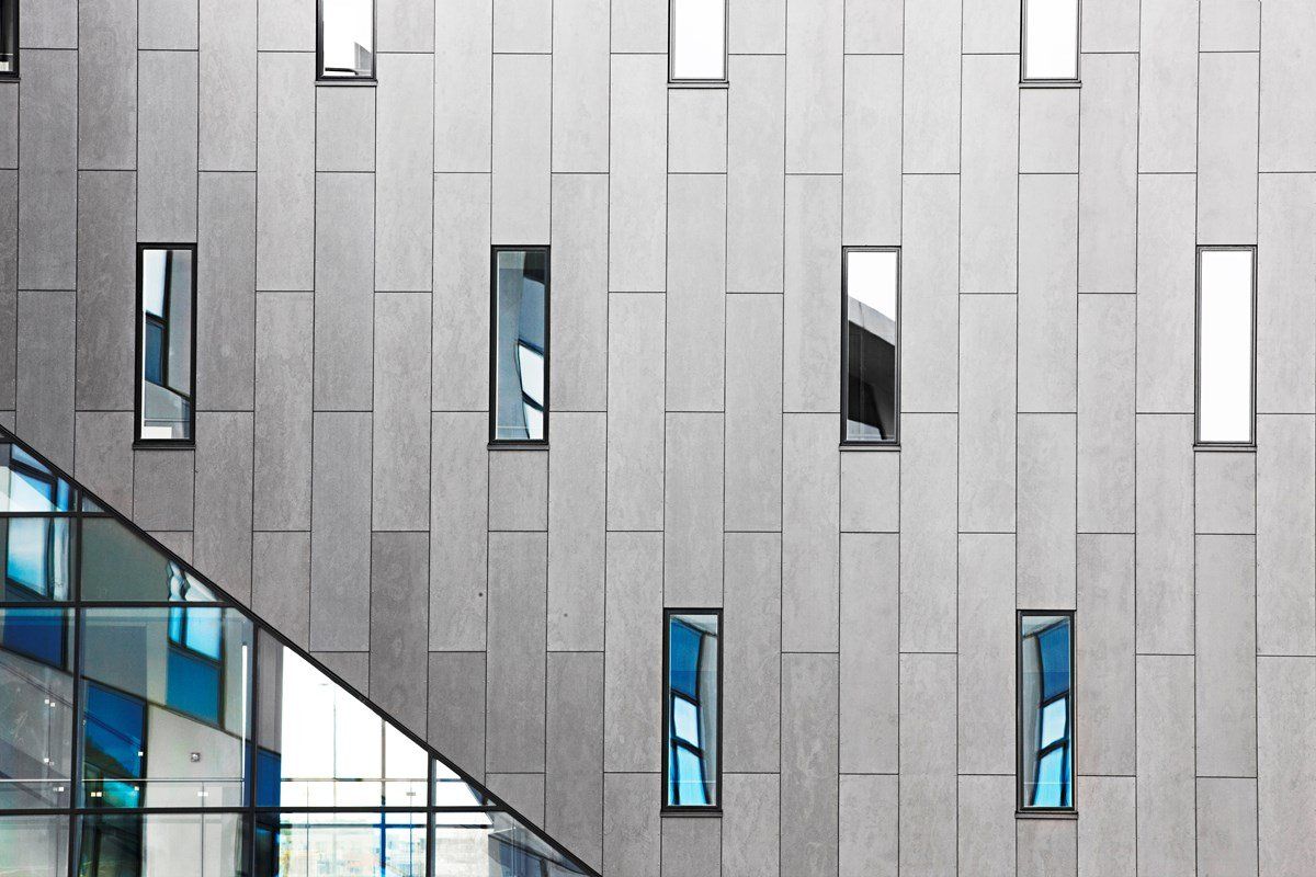 Modern building facade with rectangular windows on gray panels, blue glass corner.