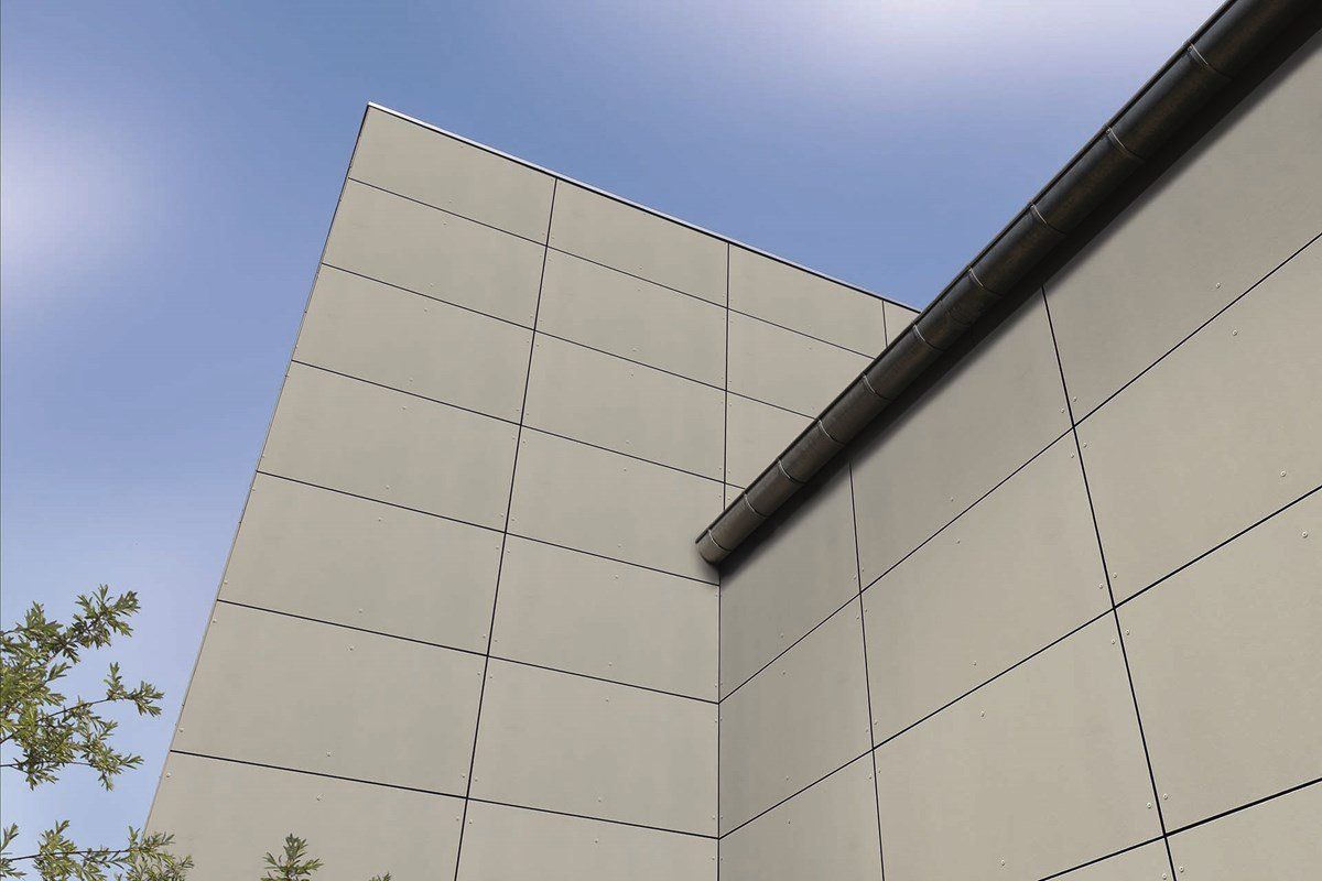 Exterior corner of a building with light gray paneling against a blue sky.
