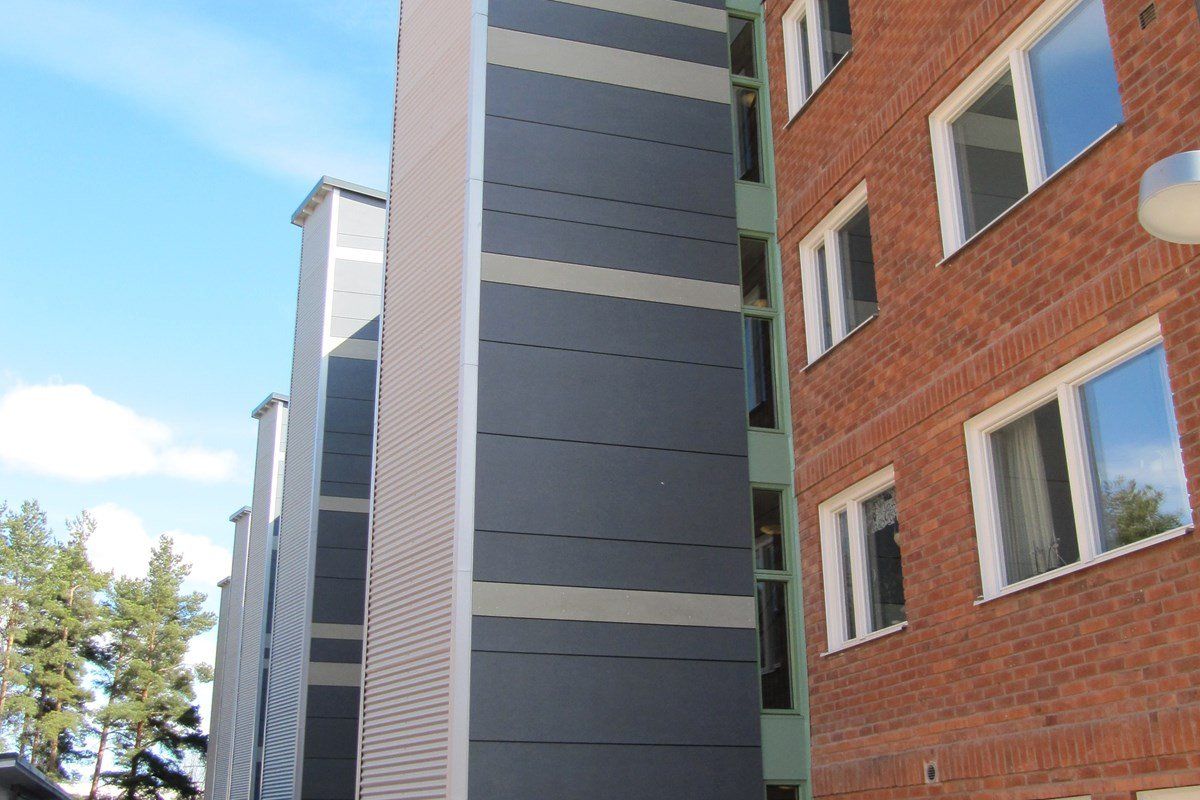 Tall apartment buildings, one brick, one with grey panels and beige trim, against a blue sky.