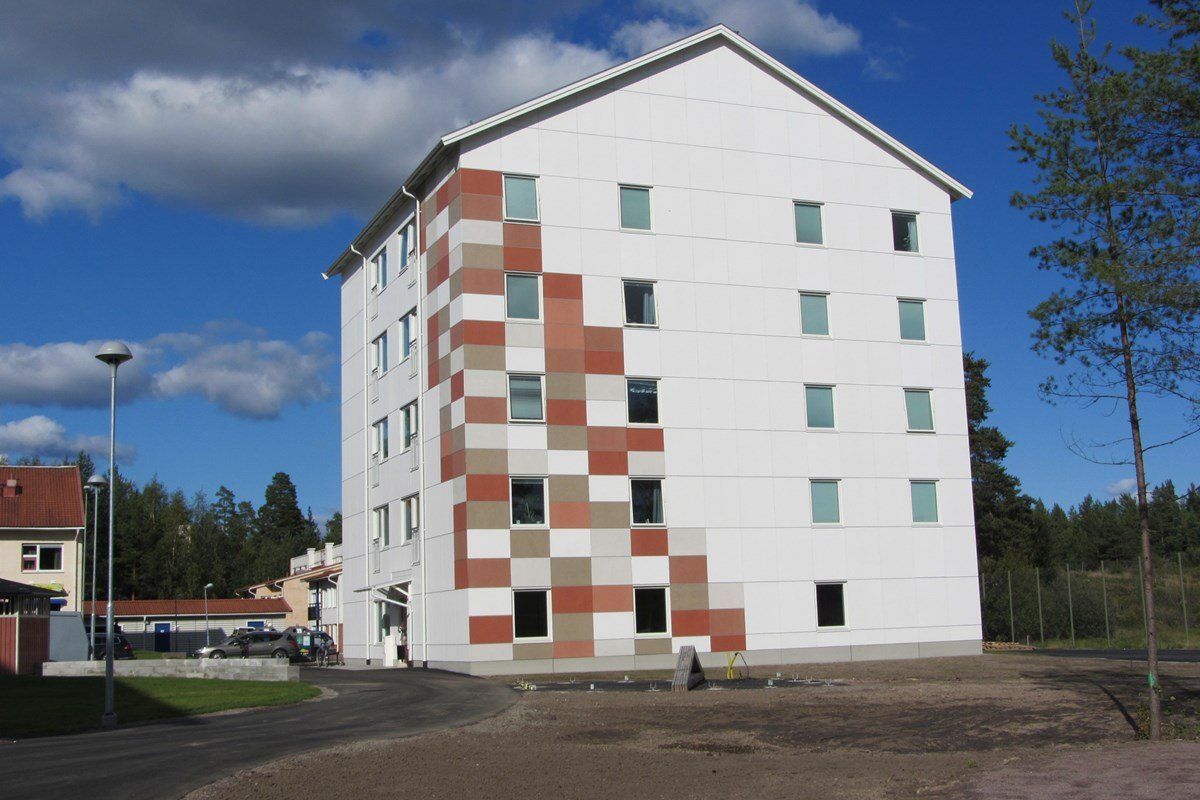 Multi-story white building with a colorful square pattern on one side. Blue sky.