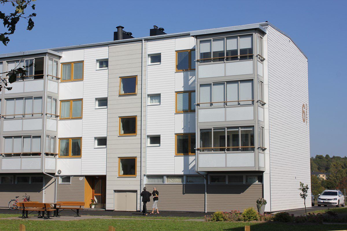 White apartment building with light gray accents, windows, and small balconies. Blue sky.