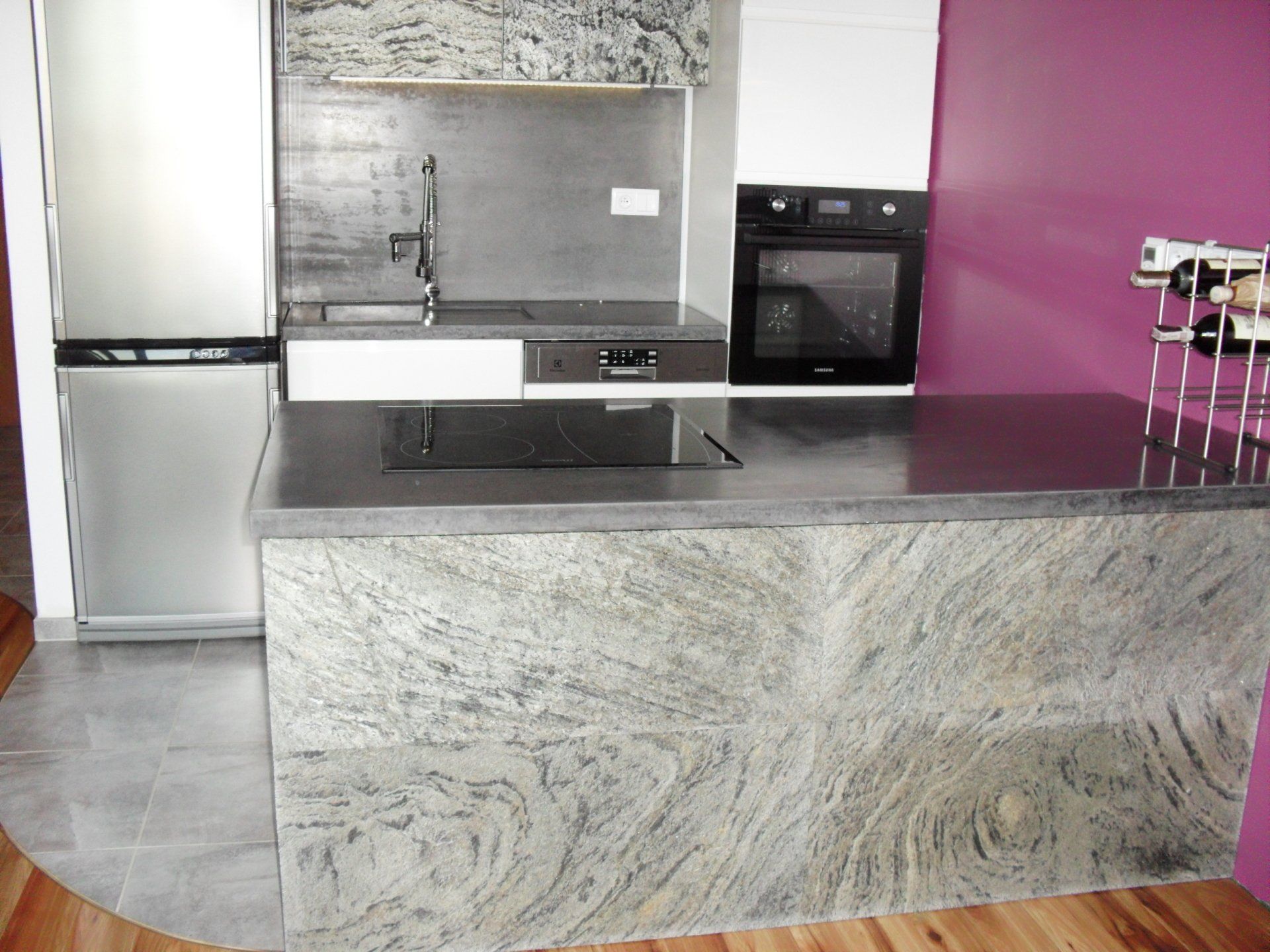 Modern kitchen with granite island, stainless steel appliances, and purple wall.