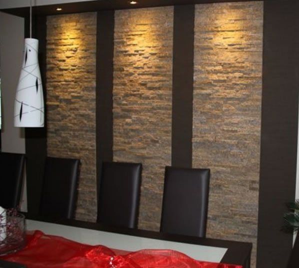 Dining room with textured stone wall, spotlights, and black chairs.