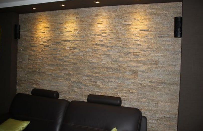 Stone accent wall with warm lighting and black speakers; a black couch sits below.