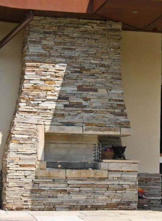 Outdoor stone fireplace with a layered design, built into a covered patio space.