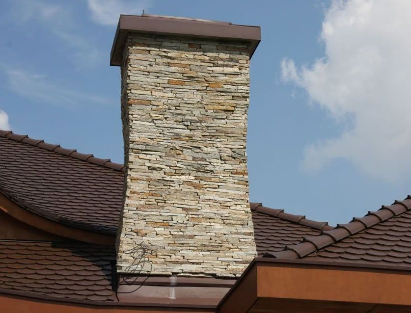 Stone chimney on a brown-tiled roof against a blue sky.