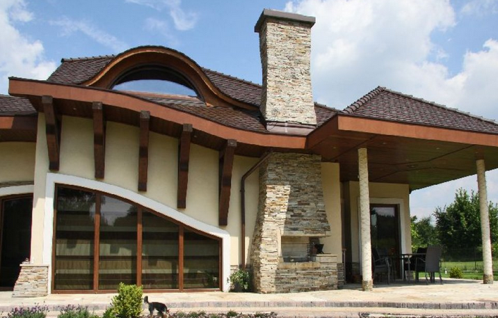 Modern house with arched roof, chimney, and stone accents against a blue sky.