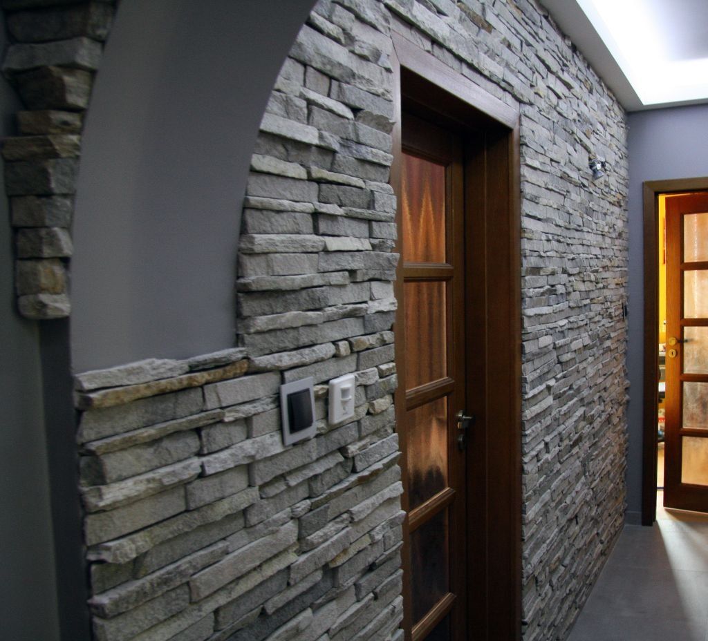 Stone-clad wall with an arched doorway, leading to a wooden door. A hallway with a second door on the right.