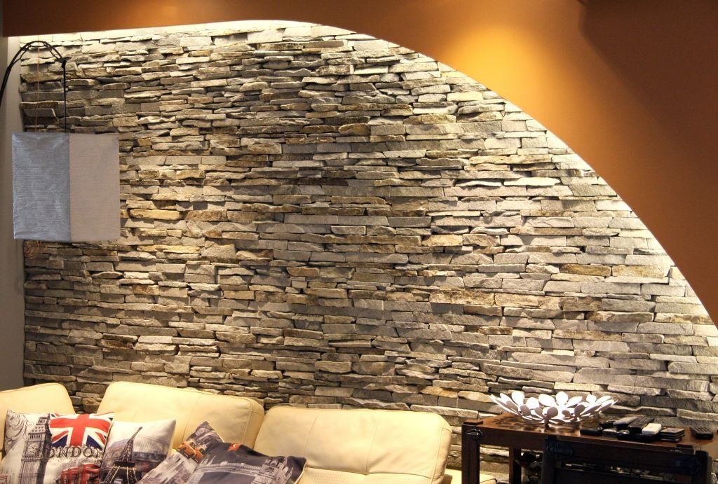 Stone wall with indirect lighting above a couch, with accent pillows.