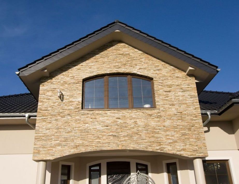 Stone facade of a house with arched window and dark roof against a clear blue sky.