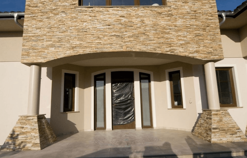 Facade of a house with stone accents, arched entryway, and dark-framed windows.