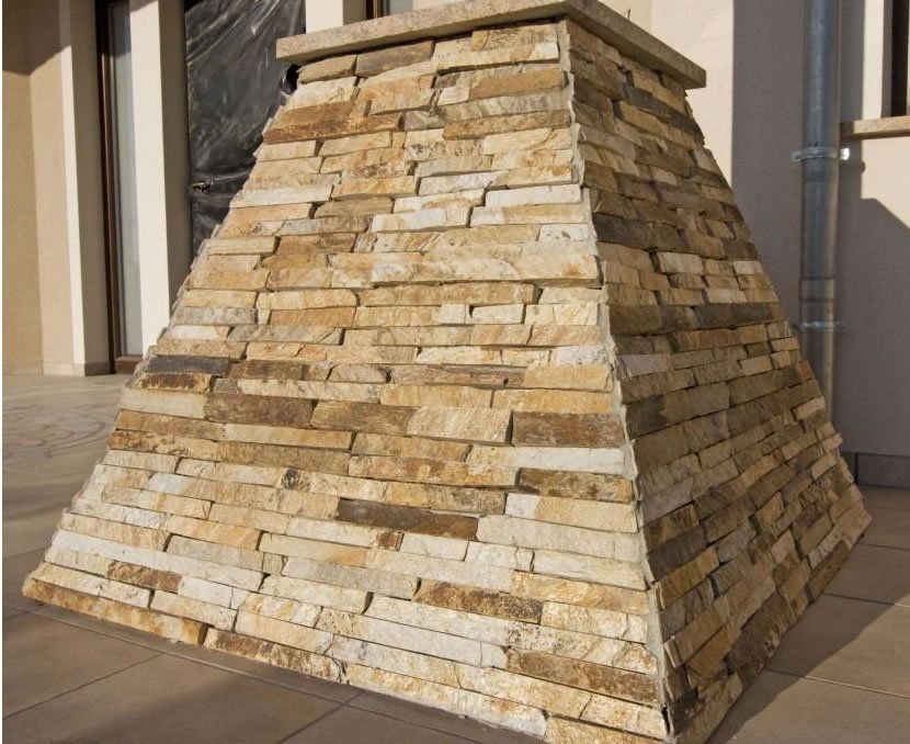 Stone-covered, pyramid-shaped structure on a patio, with a flat top and varying shades of beige and tan stone.