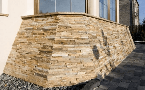 Stone-covered wall below a window; tan and brown textured bricks, with a gravel base and brick path.