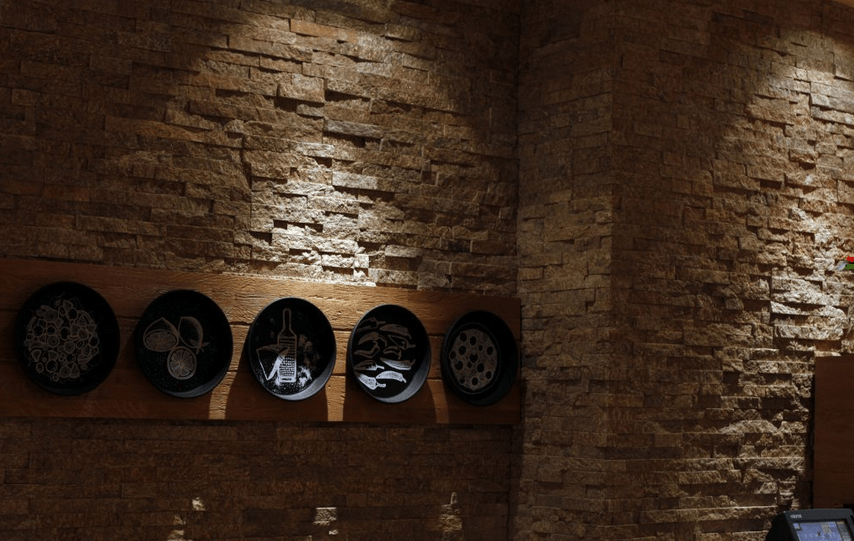 Stone wall with decorative black plates on a wooden shelf. Spotlights illuminate the wall.