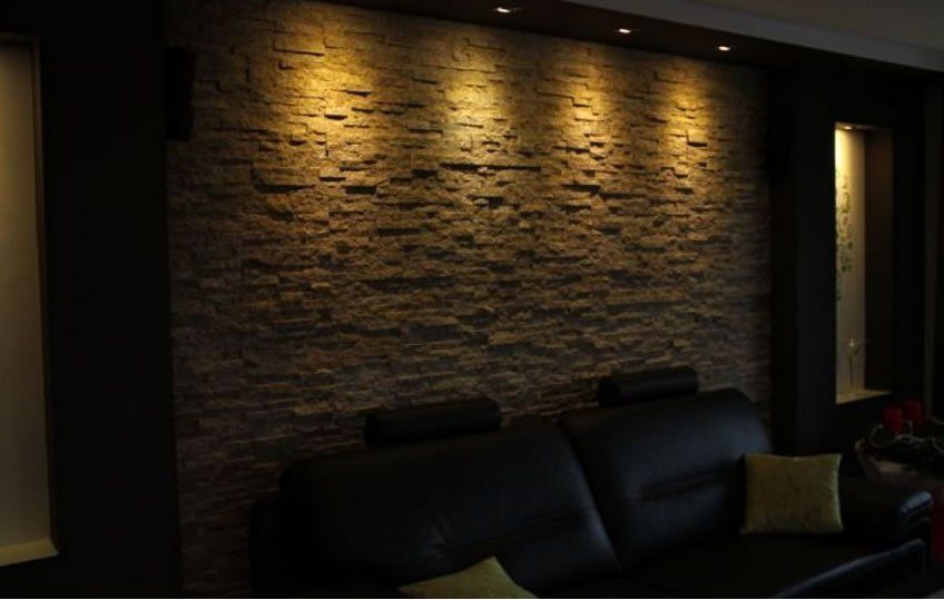 Dark living room with a stone accent wall illuminated by spotlights, above a black sofa.
