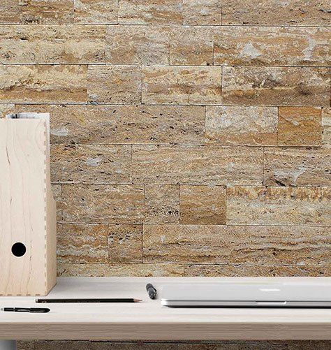 Light wooden desk with office supplies against a textured tan stone wall.