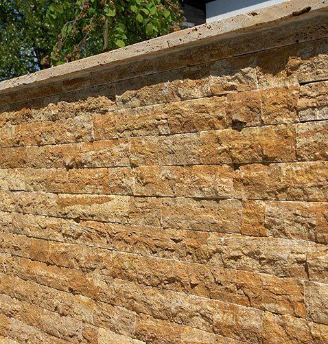 A textured, golden-brown stone wall with a concrete cap.