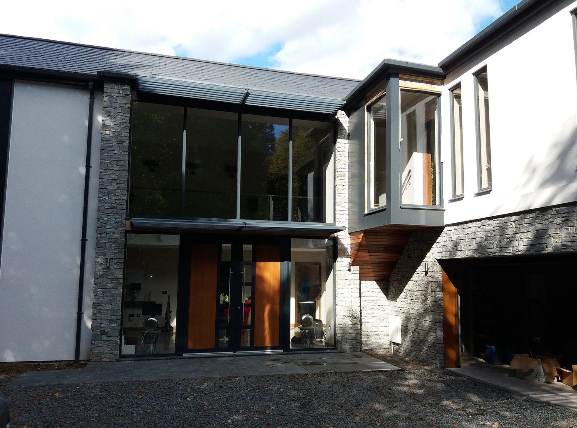 Modern home exterior with large glass windows, stone and white walls, and a small cantilevered box window.