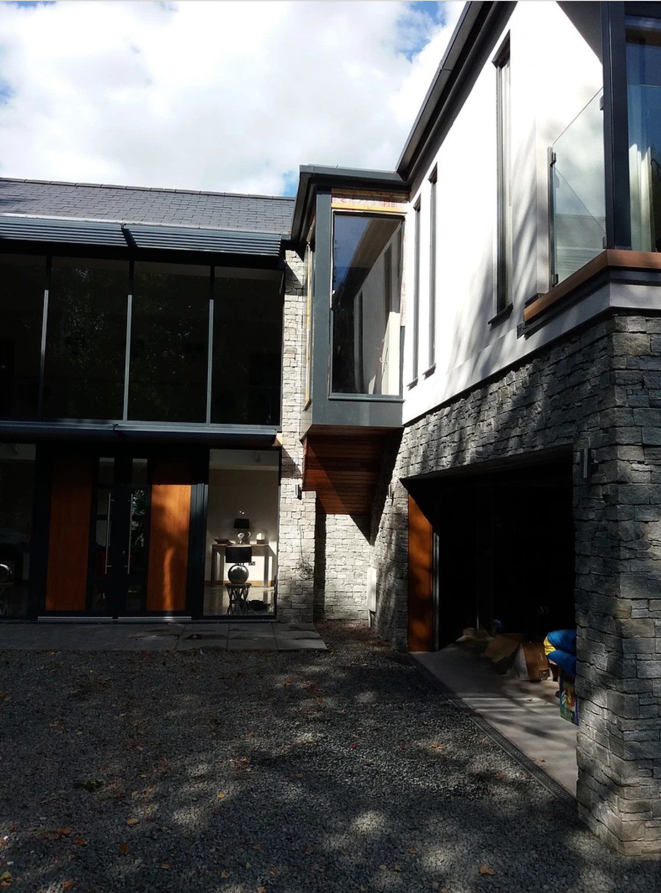 Modern house with stone and white walls, glass windows, and a cantilevered section.