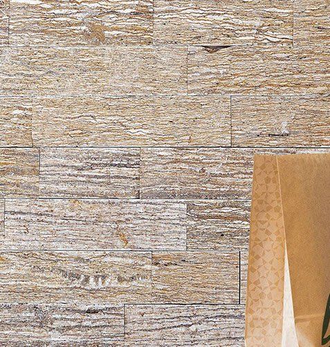 Stone tile wall with varied shades of beige and gray; partially visible brown paper.