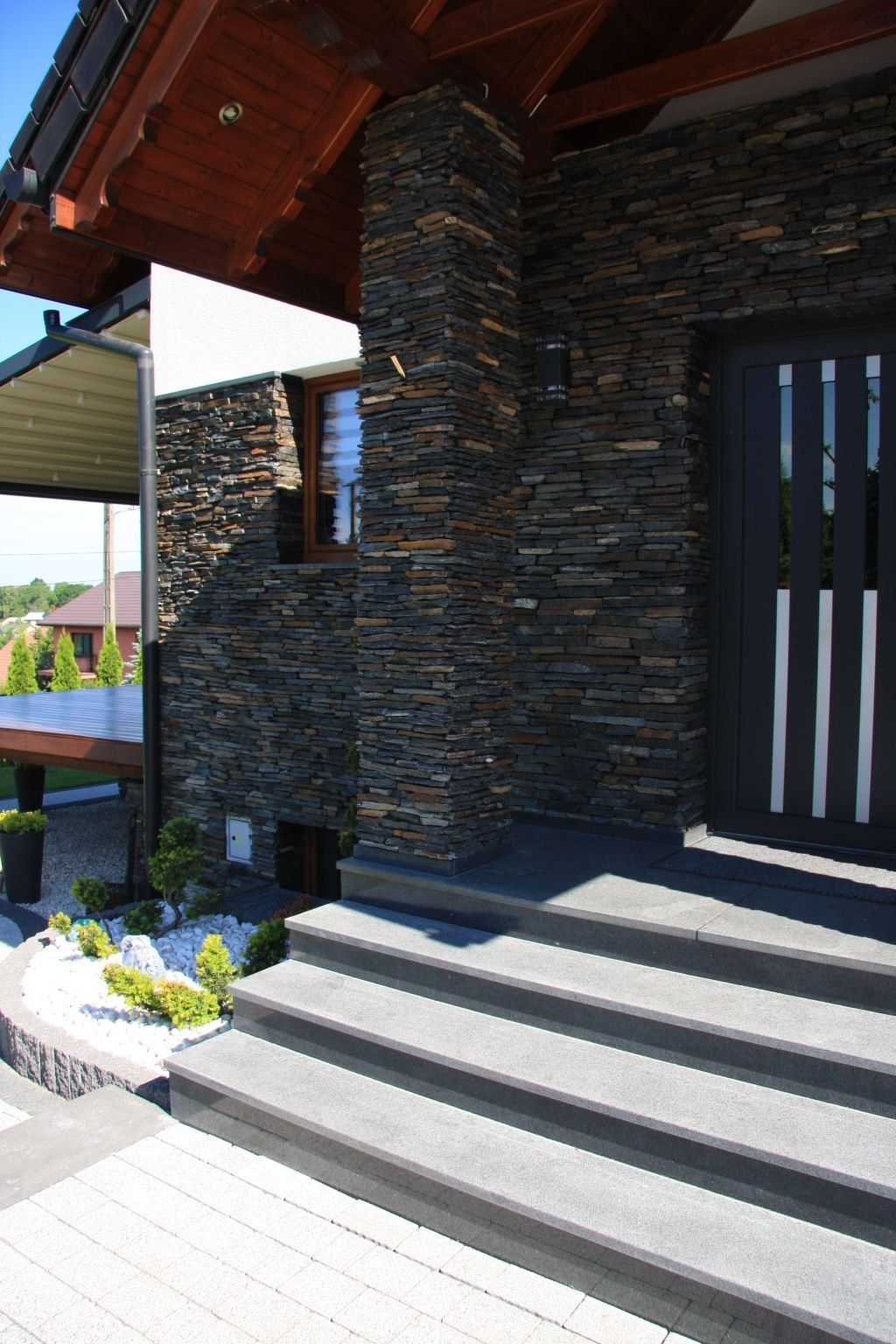 Stone-clad house exterior with dark door, steps, and landscaping.