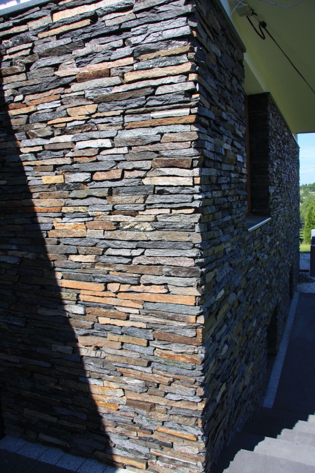 Stone exterior wall with a corner, featuring layered horizontal gray and brown stones.