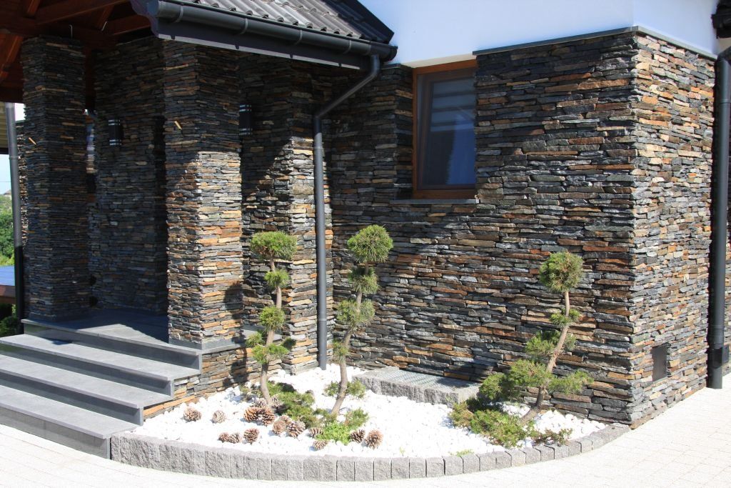 Stone-clad house exterior with small trees and white pebbles in front.