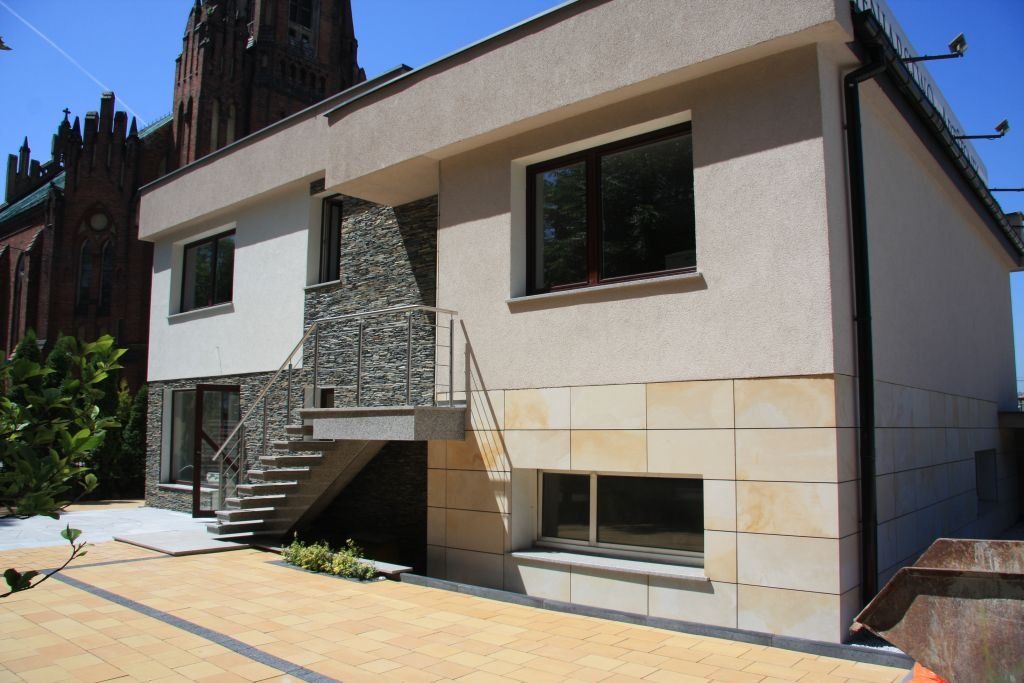 Two-story building with beige and stone facade, stairs, and dark framed windows.
