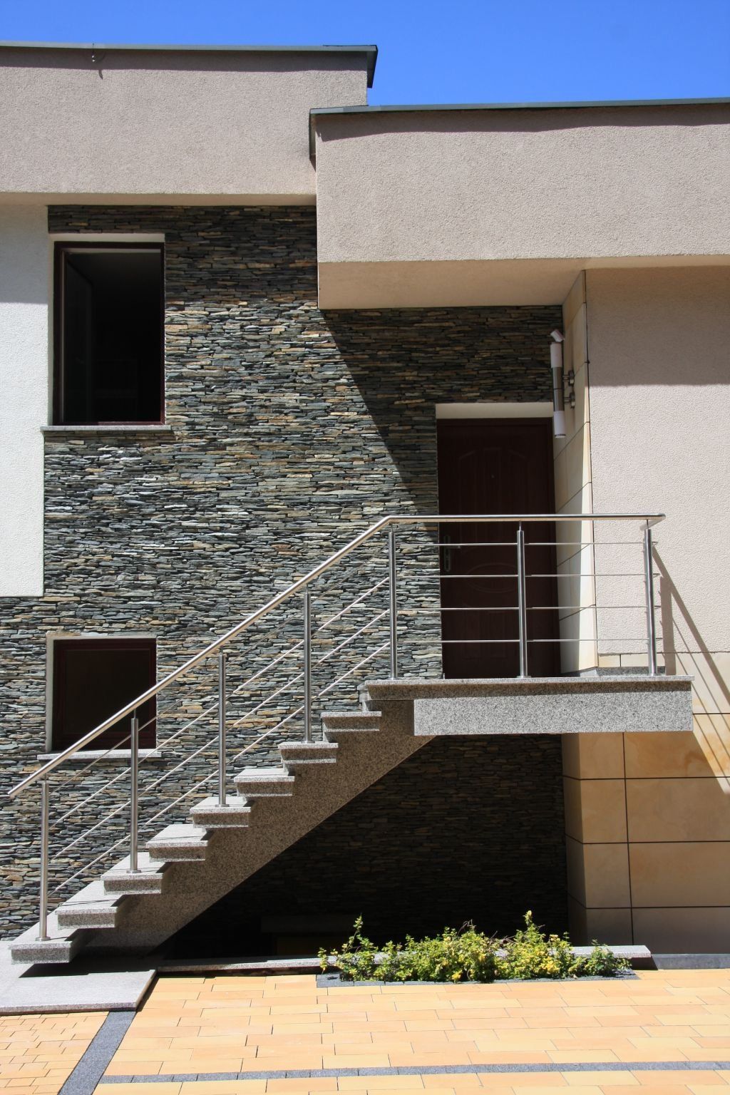 Exterior of a modern building with stone wall, stairs, and a door.
