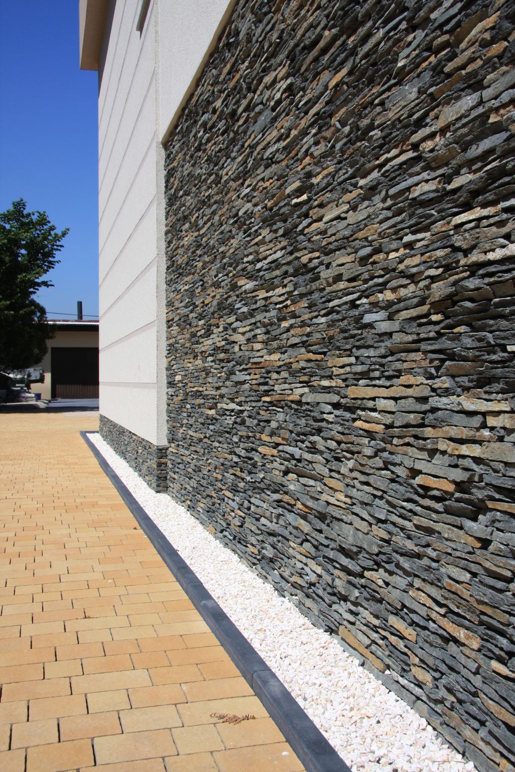 Building exterior: stone veneer wall, white building section, and tan brick walkway.