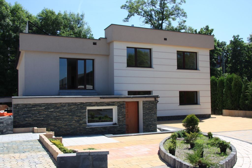 Two-story modern house with beige and white walls, dark windows, and a stone facade.