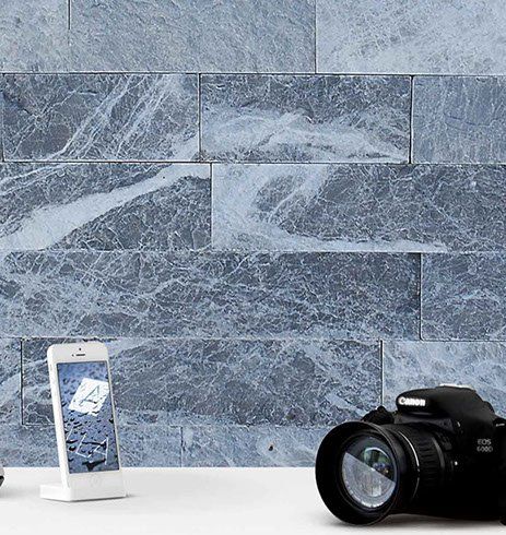 Gray marble brick wall background with a smartphone and a DSLR camera in front.