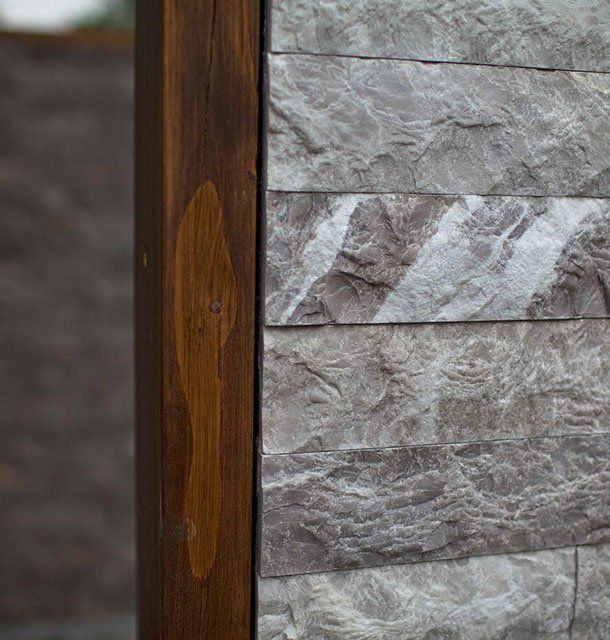 Close-up of a wooden beam next to a gray stone wall. The beam is a dark brown, with a lighter-colored, hand-shaped stain.