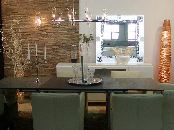 Dining room with table, chairs, chandelier, mirror, and decorative items. Stone wall backdrop.