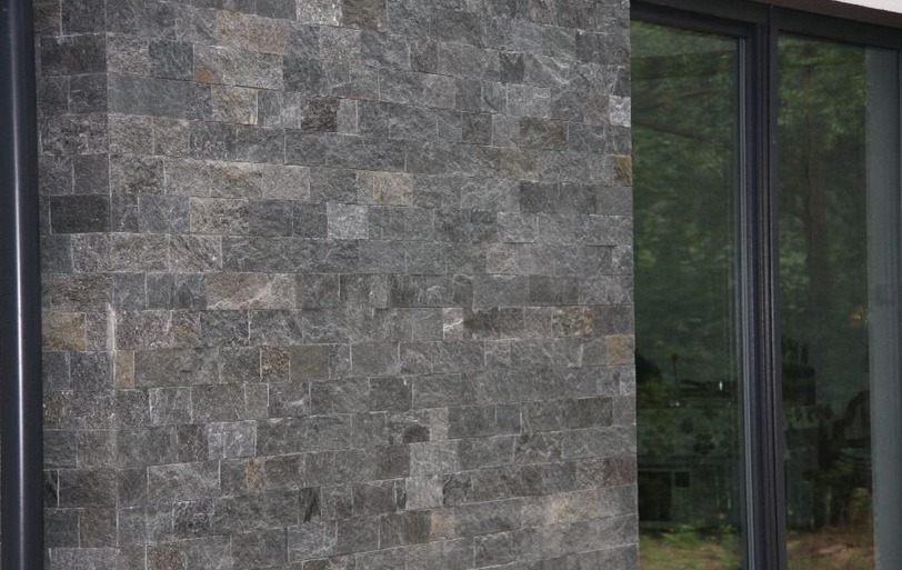 Dark gray stone wall next to a large window with reflective glass.