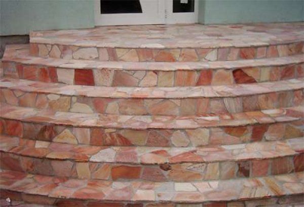 Curved outdoor steps covered in reddish-brown flagstone lead to a white door.