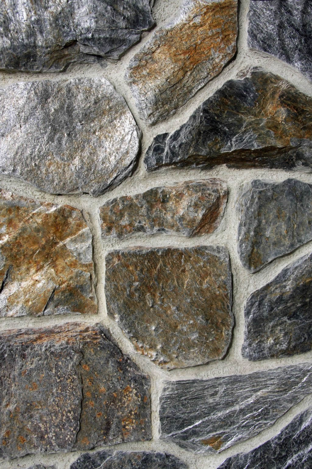 Close-up of a stone wall with gray, brown, and tan rocks joined by white mortar.
