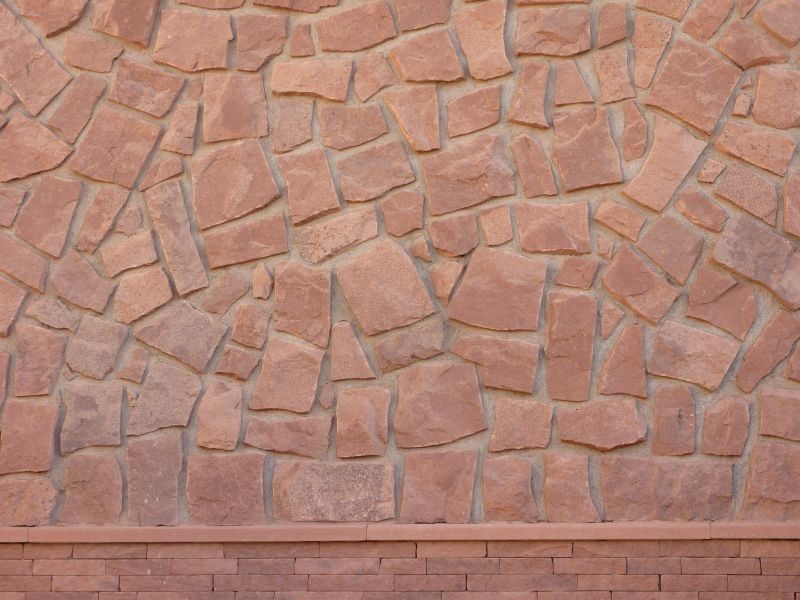 Stone wall with reddish-brown blocks, laid in an irregular pattern, above a darker stone base.