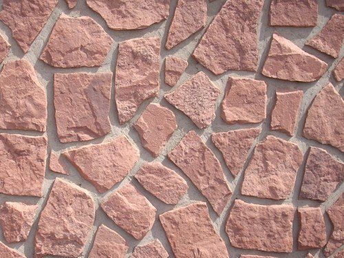 Red stone wall with irregular shaped stones and gray mortar.