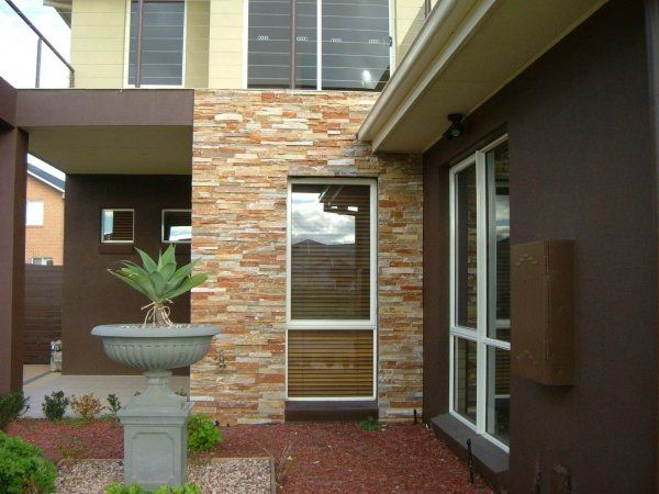 Brown and tan brick exterior of a modern house with a tall vertical window and decorative stone wall.