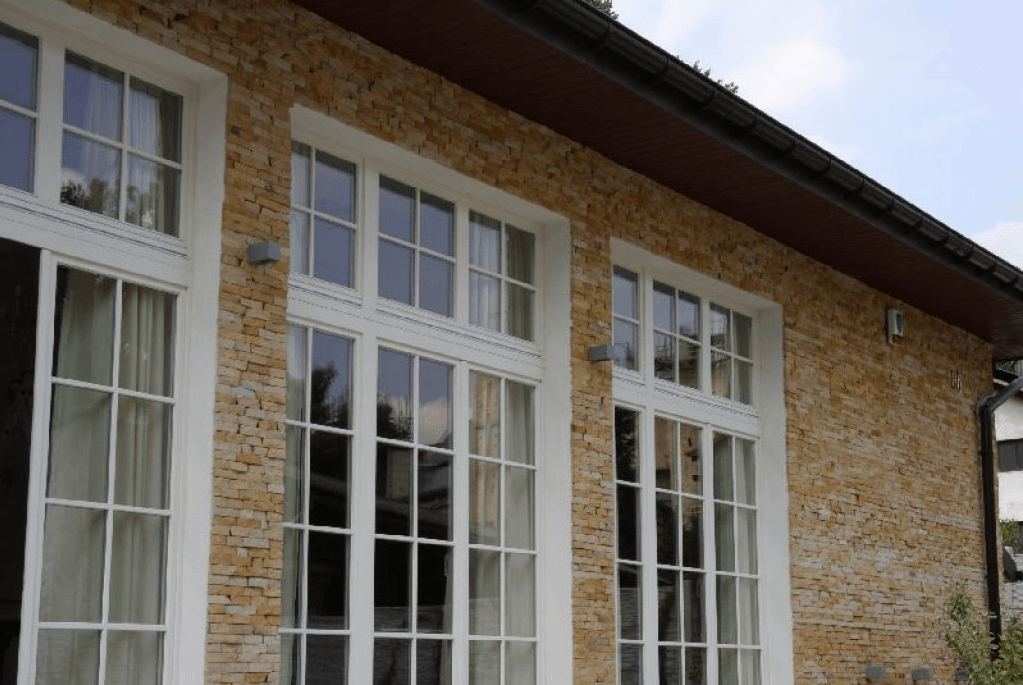 Exterior of a building with white framed windows against a beige stone wall.