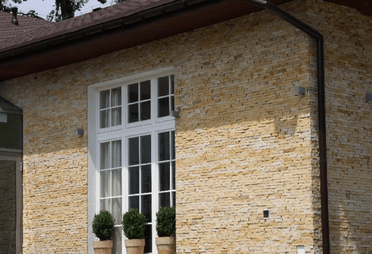Exterior wall with stacked stone facade and white-framed window.