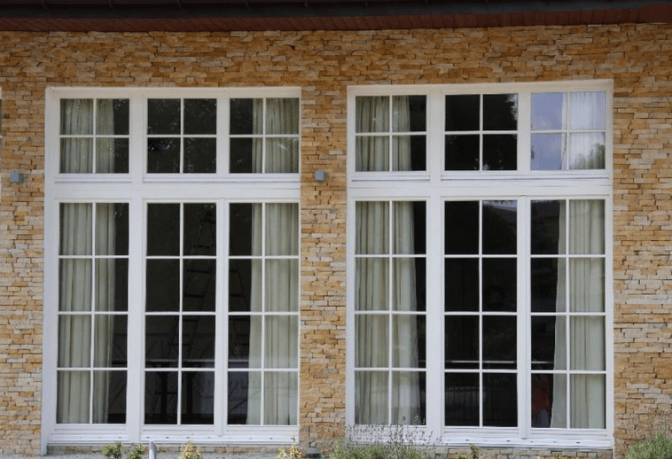 Two white-framed windows with multiple panes against a light-brown brick wall, one window slightly open at the top.
