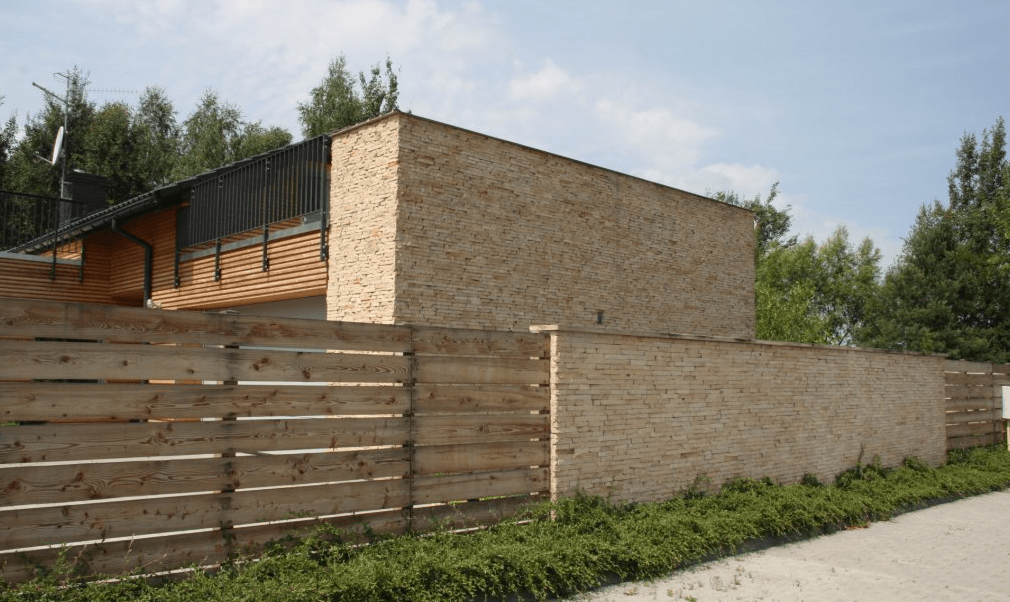 Wooden fence in front of a modern brick building, with trees in the background under a blue sky.