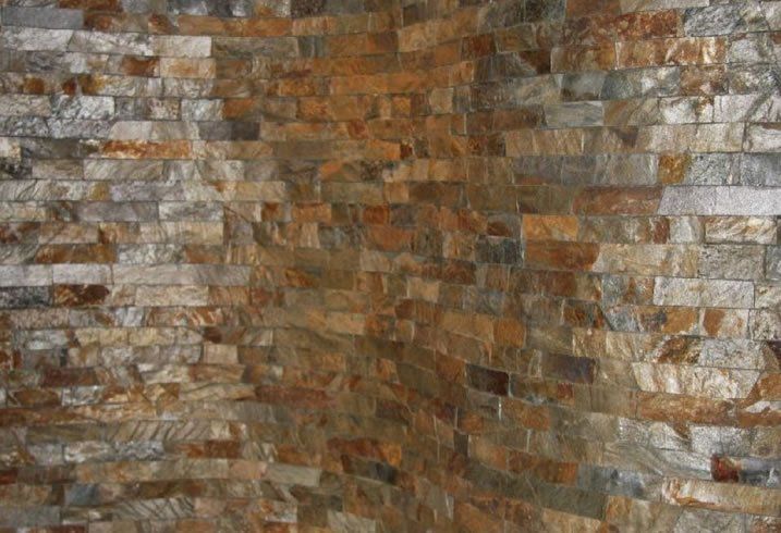 Corner of a wall covered in textured, rectangular stone tiles in shades of brown, gray, and gold.